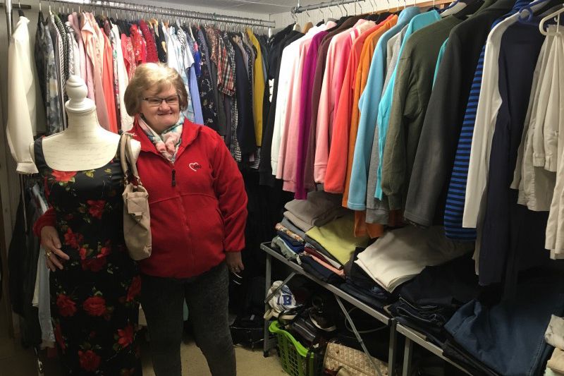 Frau steht in einem Raum voller Klamotten und lächelt.