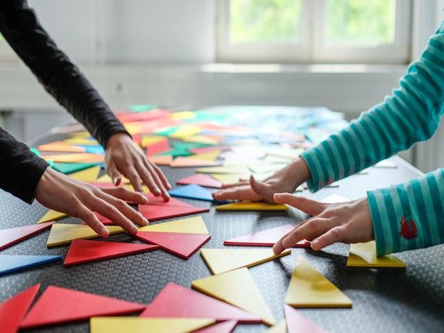 Hände spielen gemeinsam ein Geometrie-Spiel.