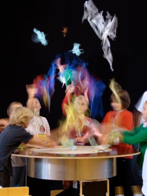 Kinder werfen bunte Tücher in die Luft.